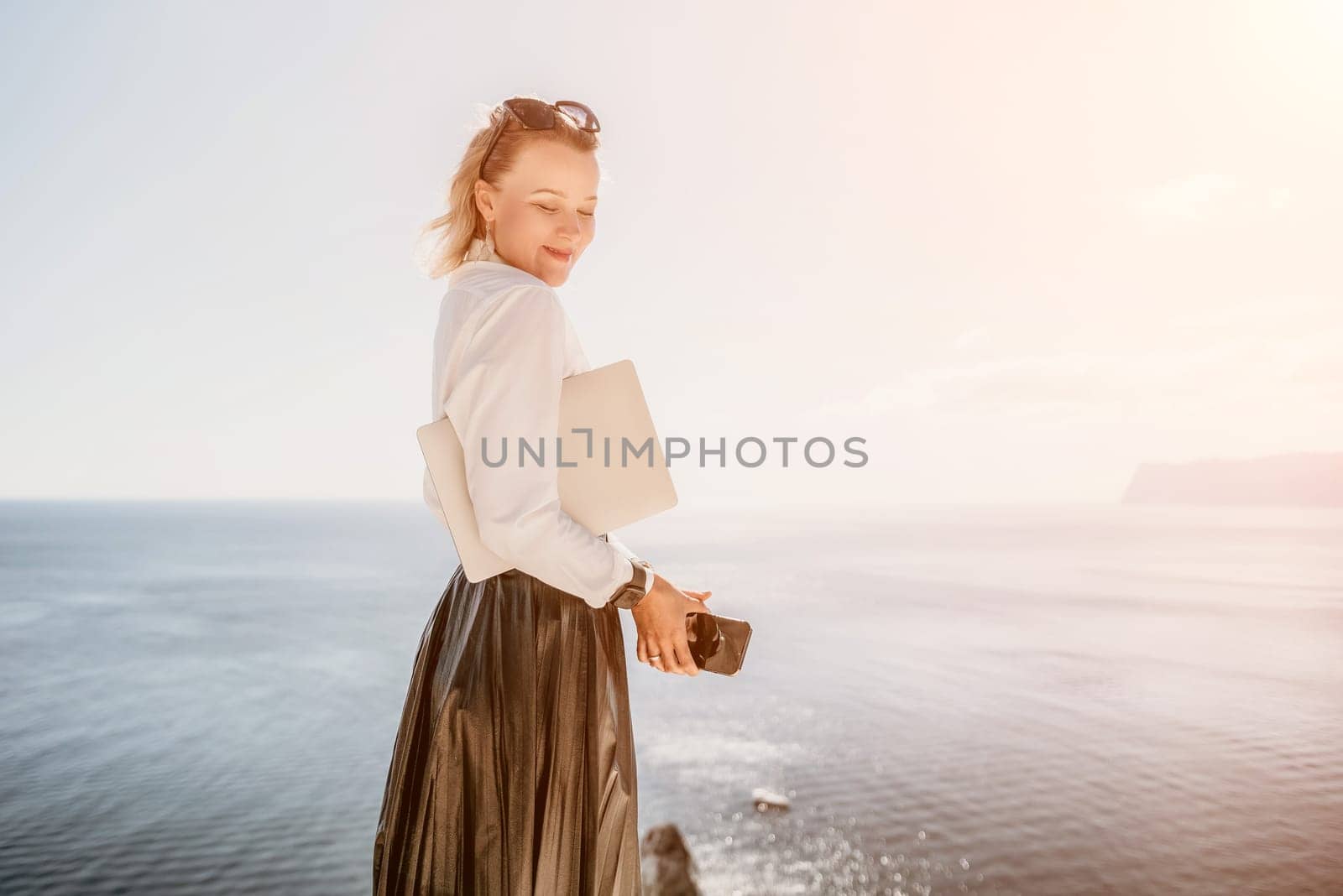 Digital nomad, Business woman working on laptop by the sea. Pretty lady typing on computer by the sea at sunset, makes a business transaction online from a distance. Freelance remote work on vacation