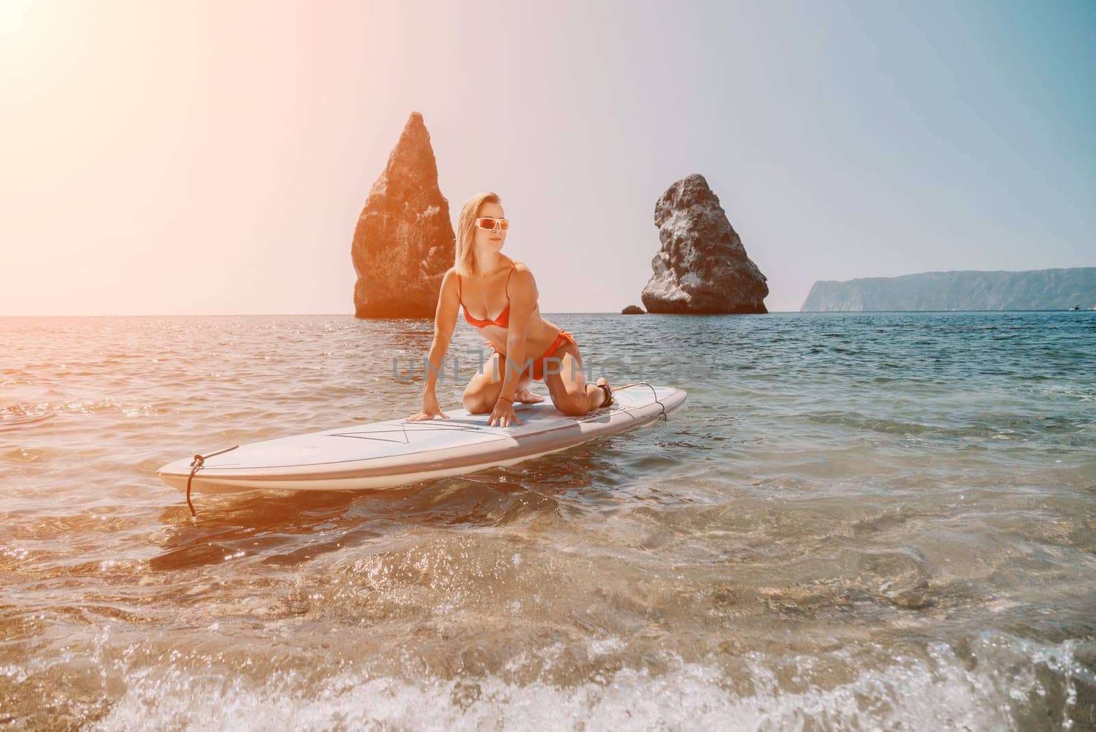 Woman sea sup. Close up portrait of happy young caucasian woman with blond hair looking at camera and smiling. Cute woman portrait in red bikini posing on sup board in the sea by panophotograph