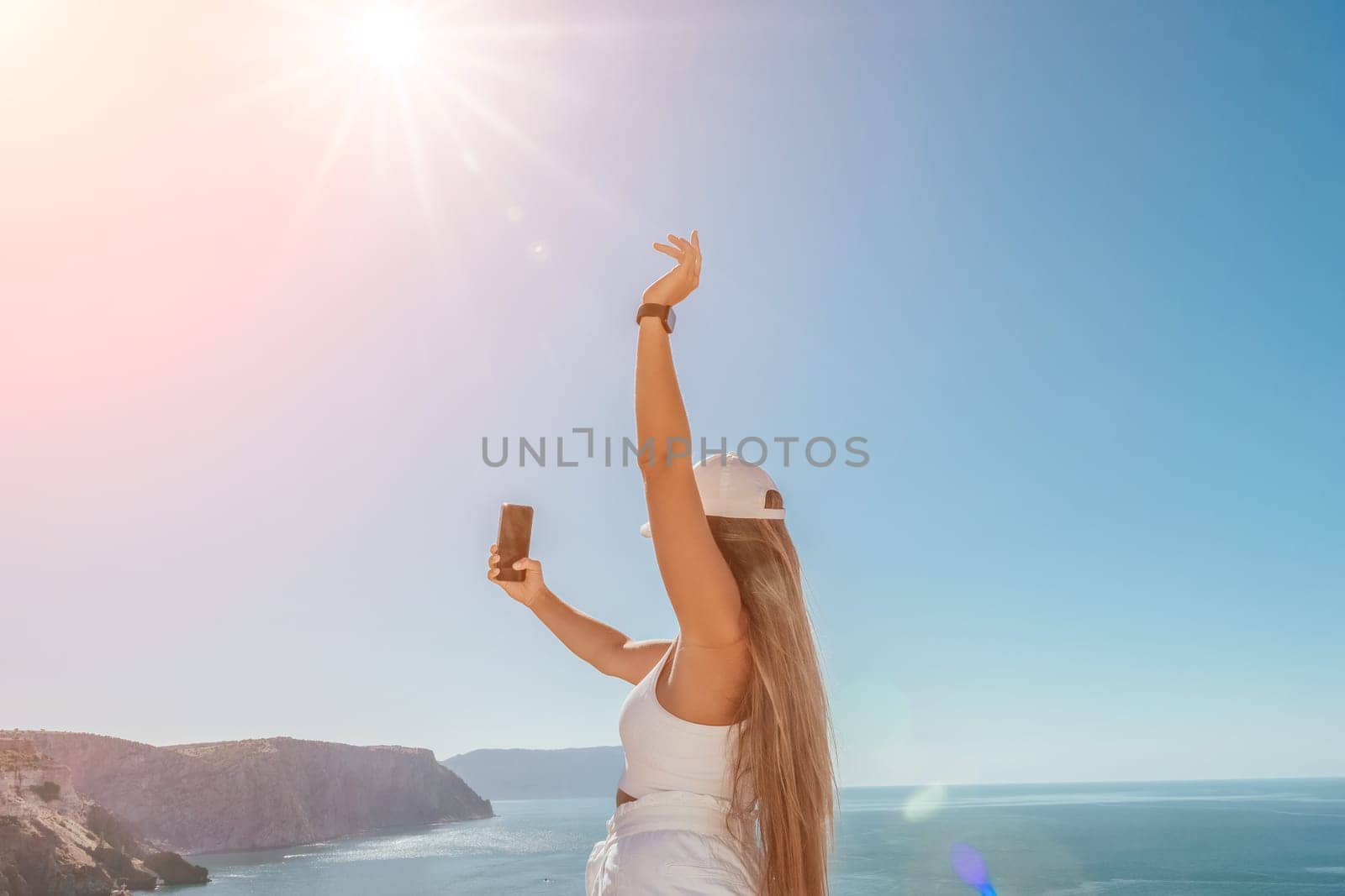 Digital nomad, woman in the hat, a business woman with a laptop sits on the rocks by the sea during sunset, makes a business transaction online from a distance. Freelance, remote work on vacation. by panophotograph