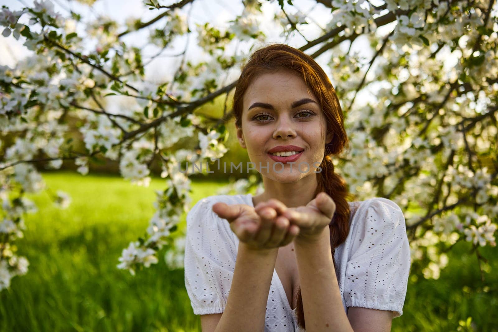 openly smiling woman against the backdrop of a flowering tree stretches her palms to the camera by Vichizh