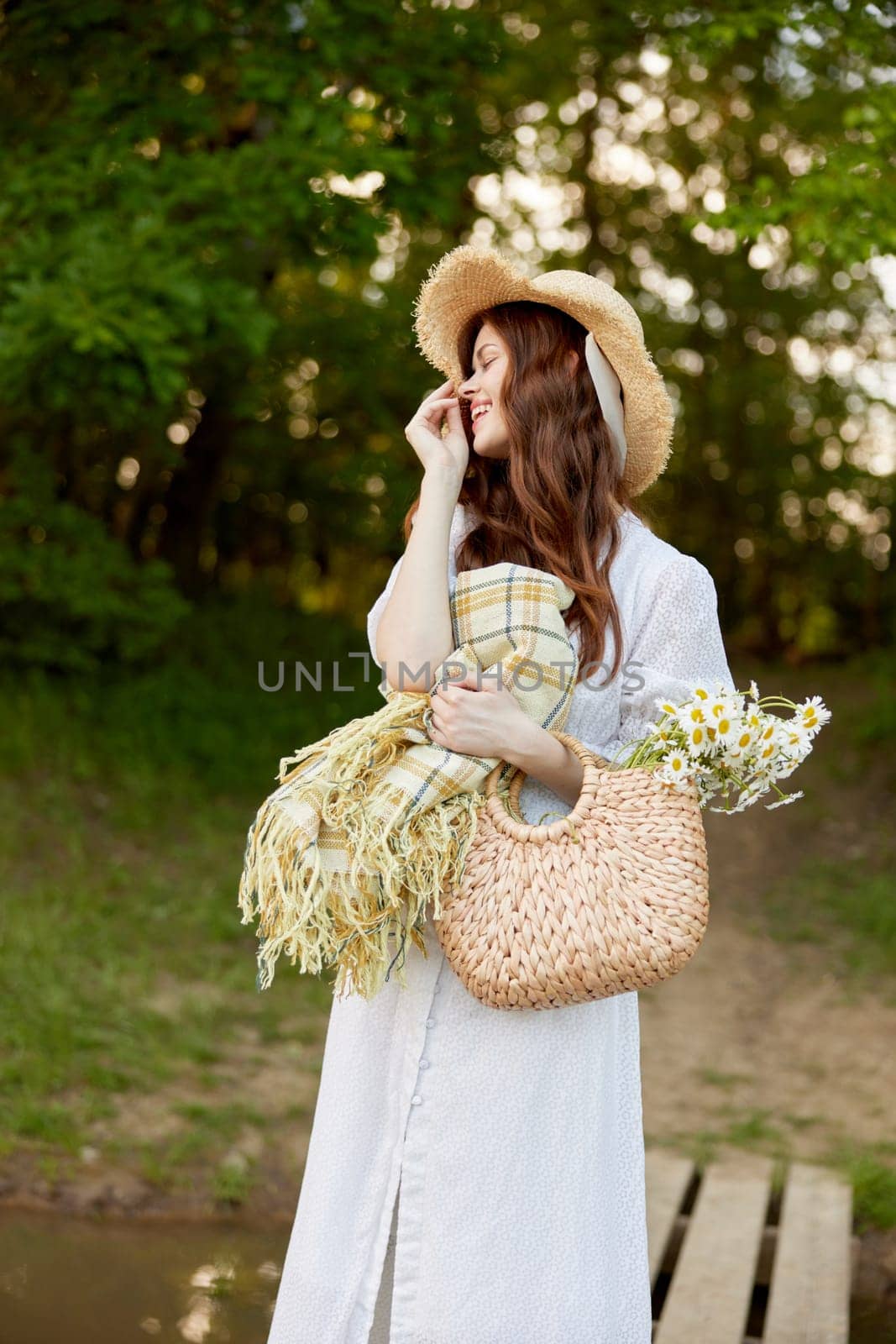 portrait of a cute woman in a wicker hat, light dress and with a plaid in her hands resting in nature. High quality photo