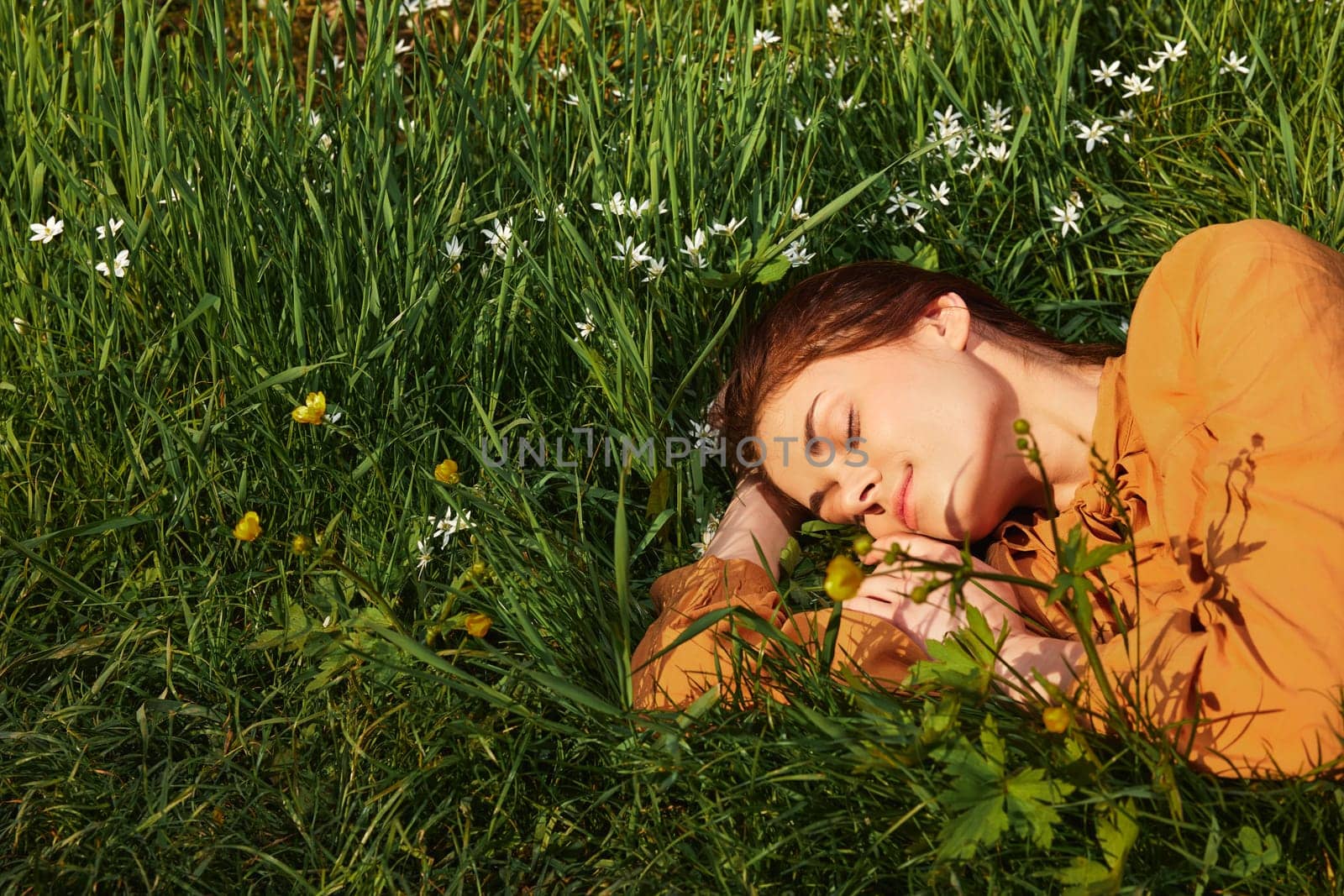 a close horizontal photo of a happy woman lying in the grass with her eyes closed and a pleasant smile on her face. High quality photo