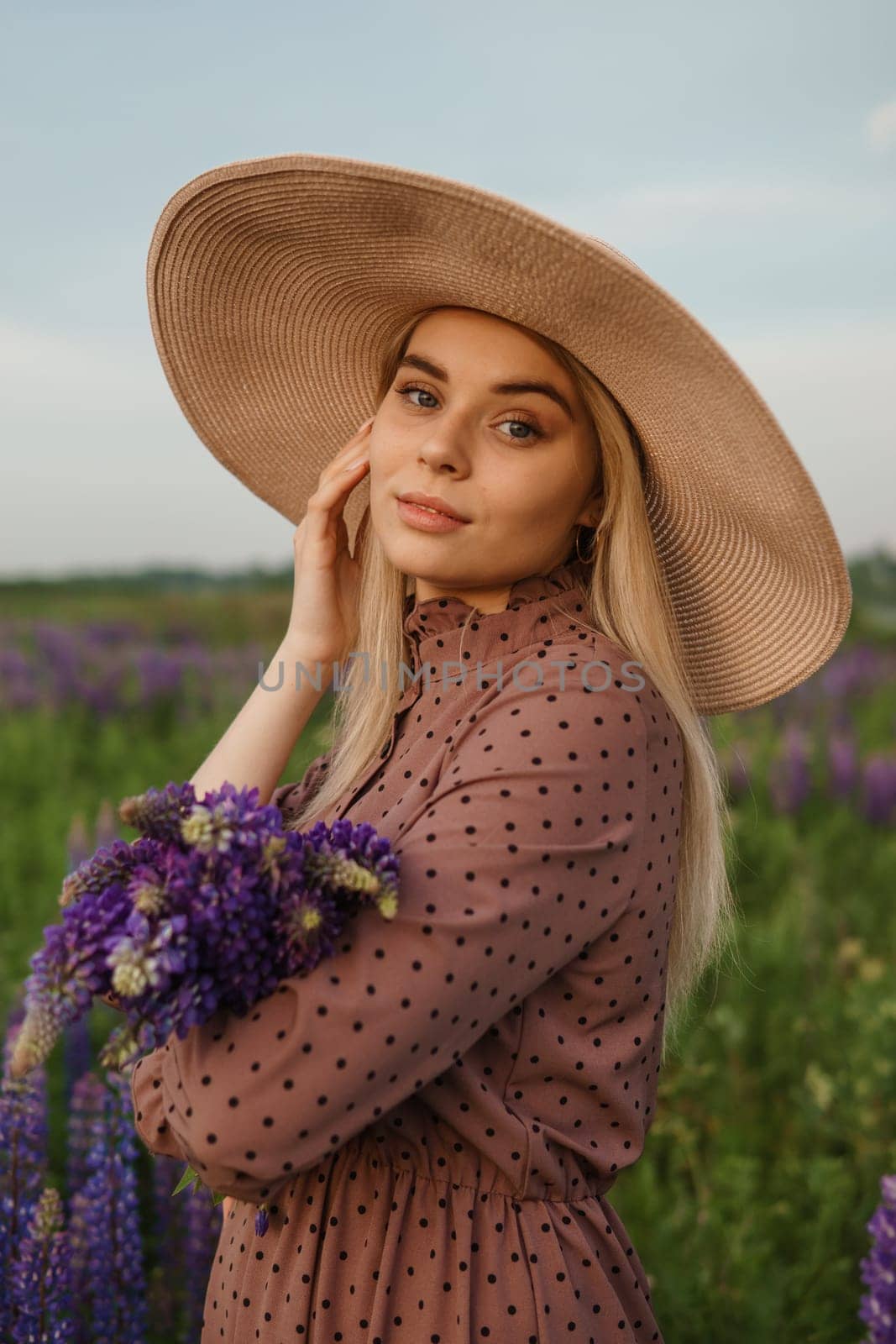 A beautiful woman in a straw hat walks in a field with purple flowers. A walk in nature in the lupin field by Annu1tochka