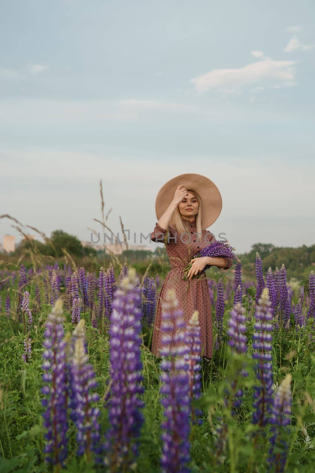 A beautiful woman in a straw hat walks in a field with purple flowers. A walk in nature in the lupin field by Annu1tochka