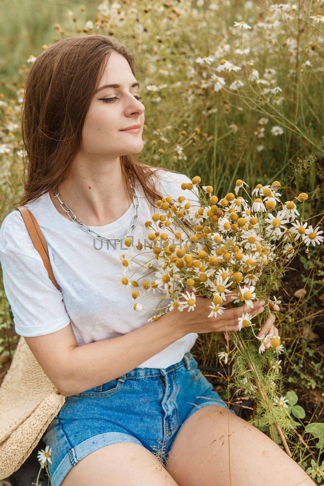 Beautiful young woman in nature with a bouquet of daisies. Field daisies, field of flowers. Summer tender photo.