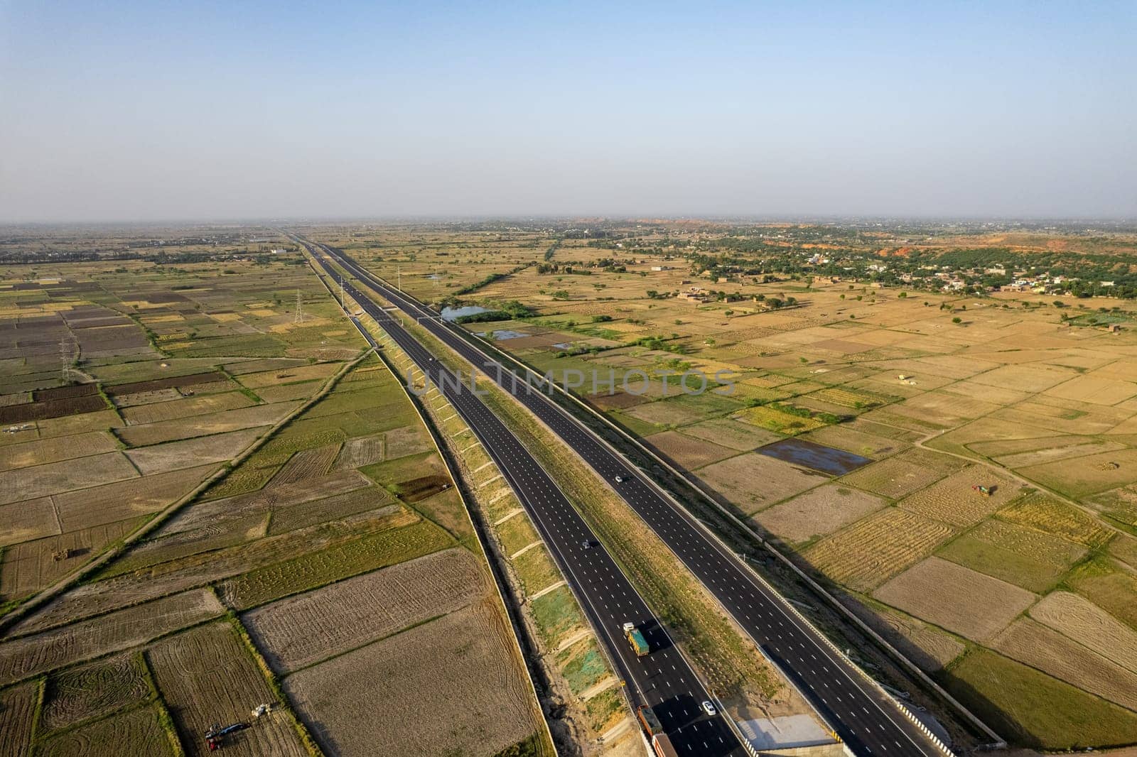 locked tripod aerial drone shot of new delhi mumbai jaipur express elevated highway showing six lane road with green feilds with rectangular farms on the sides