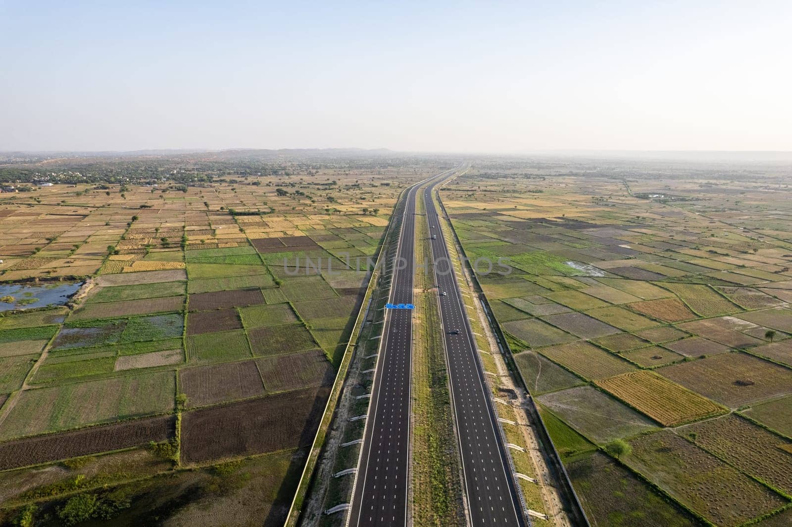 orbit aerial drone shot of new delhi mumbai jaipur express elevated highway showing six lane road with green feilds with rectangular farms by Shalinimathur