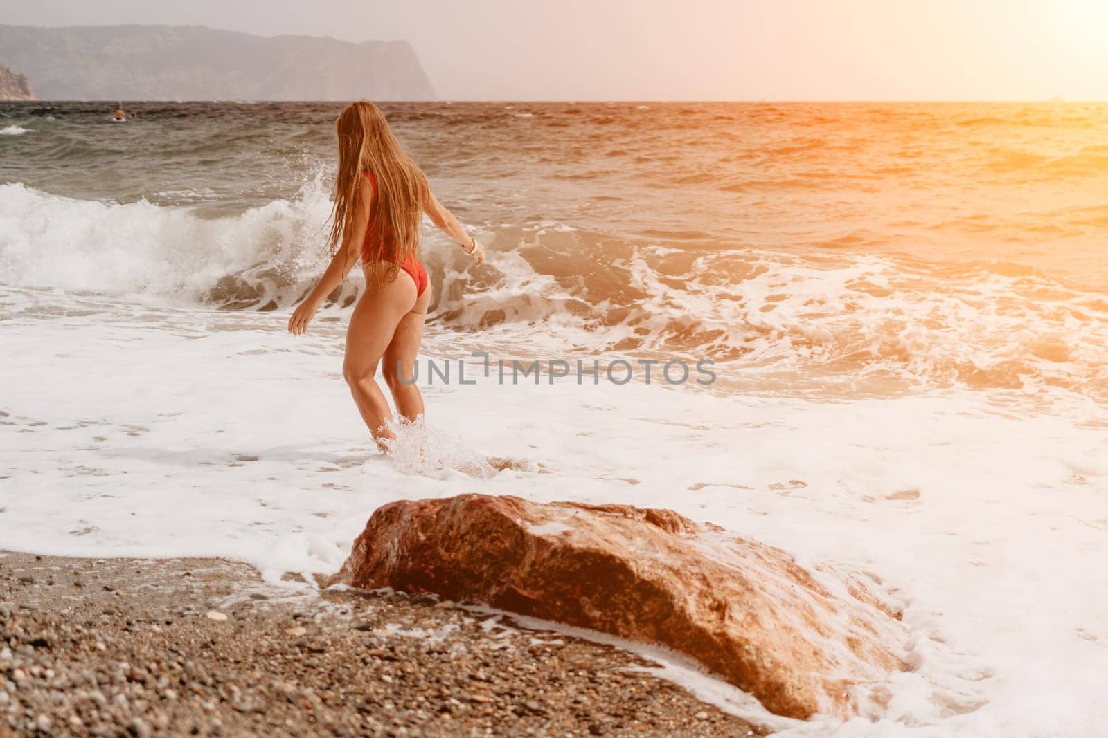Woman summer travel sea. Happy tourist in red bikini enjoy taking picture outdoors for memories. Woman traveler posing on beach at sea surrounded by volcanic mountains, sharing travel adventure joy by panophotograph