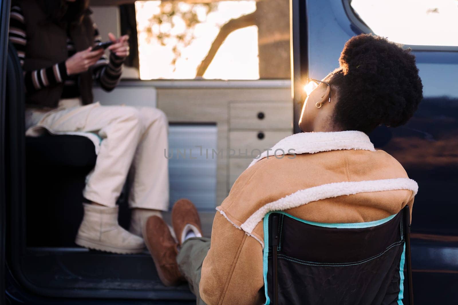 two unrecognizable young women relaxing sitting in a camper van at sunset, concept of road trip travel and adventure with best friend