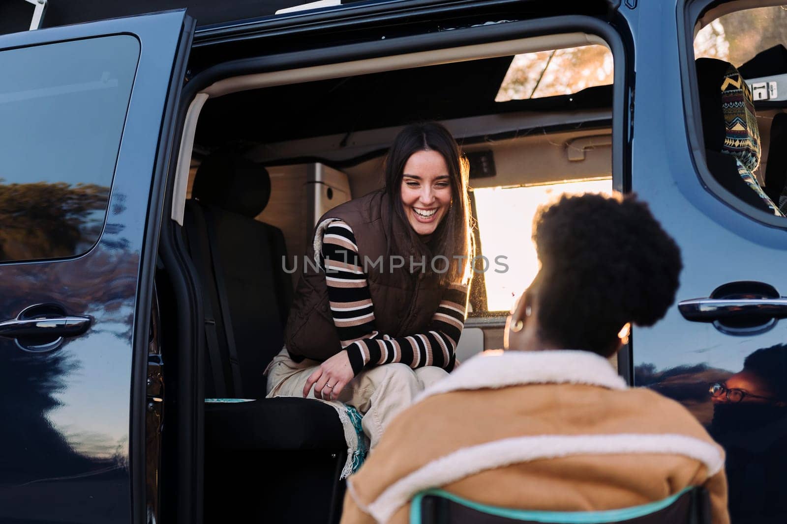 two young women chatting and having fun in a camper van at sunset, concept of travel adventure and weekend getaway with best friend