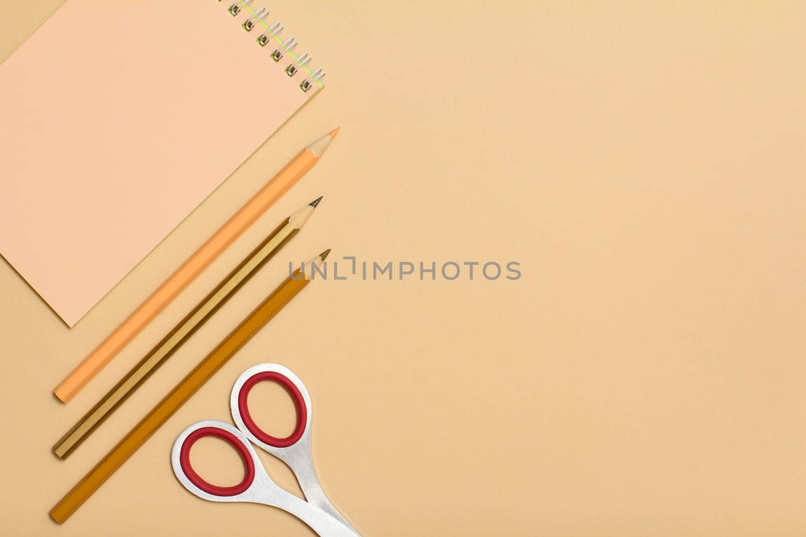 School supplies. Notebook, color pencils and scissorson on beige background. Top view with copy space. Back to school concept. Pastel colors.