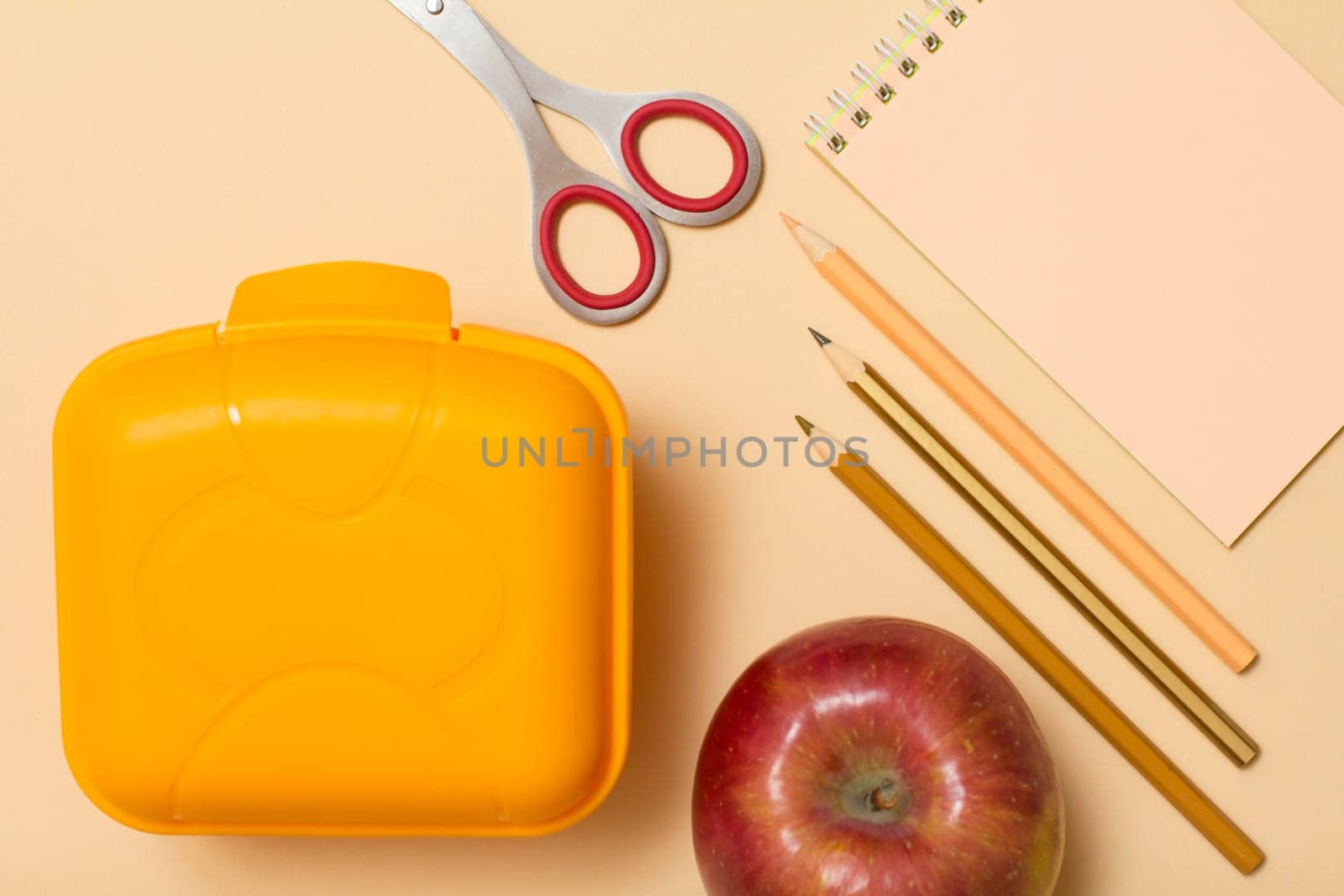 School supplies. Notebook, color pencils, apple, scissors and lunch box on beige background. Top view. Back to school concept. Pastel colors
