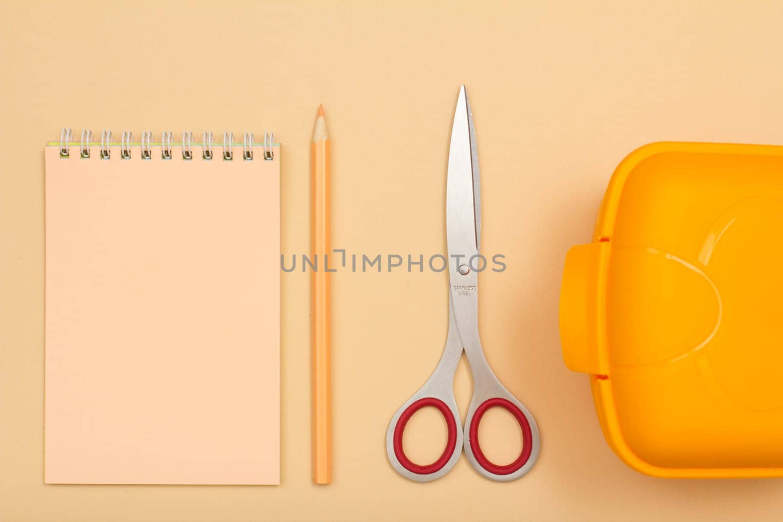 School supplies. Notebook, color pencil, scissors and lunch box on beige background. Top view. Back to school concept. Pastel colors.
