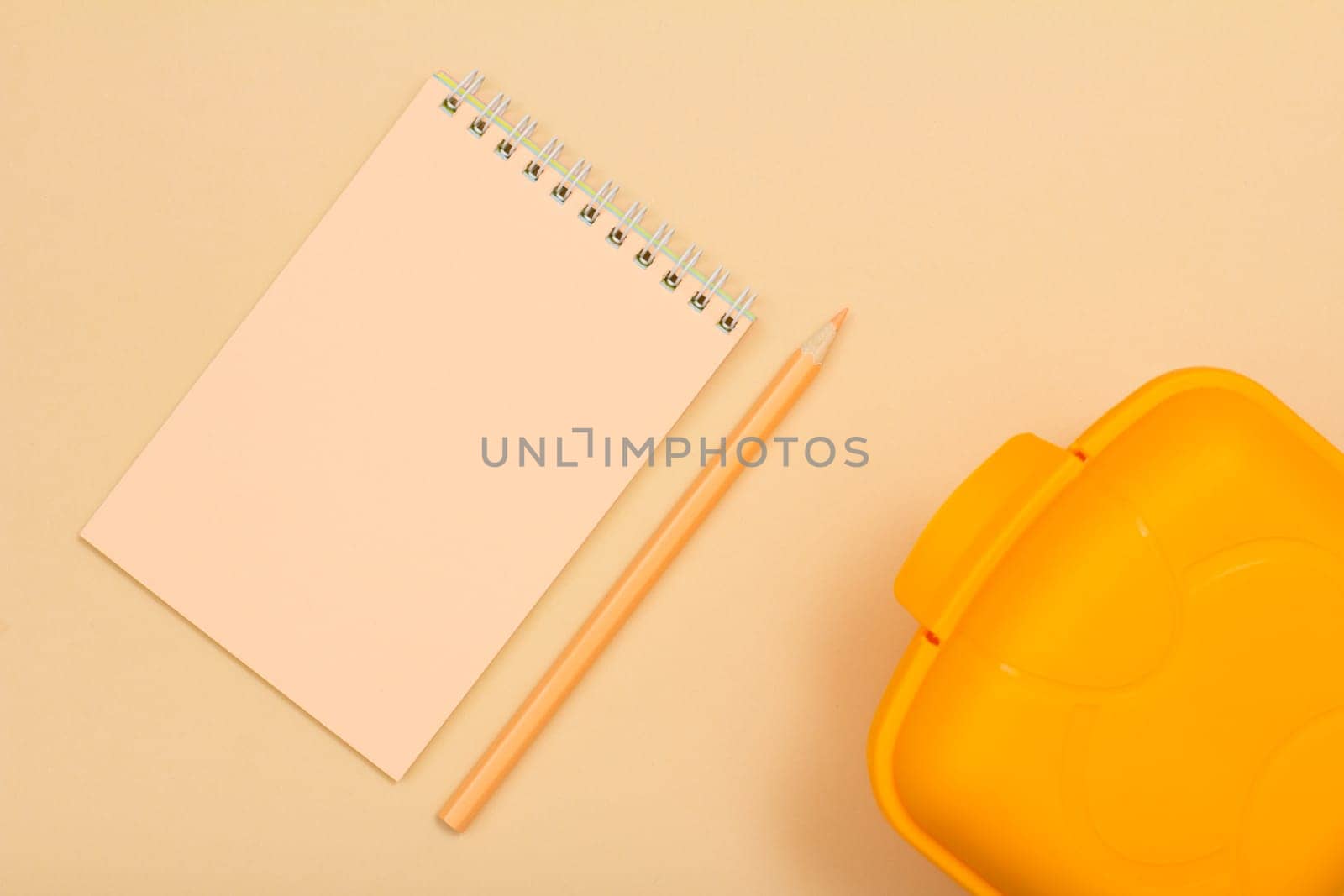 School supplies. Notebook, color pencil and lunch box on beige background. Top view. Back to school concept. Pastel colors.