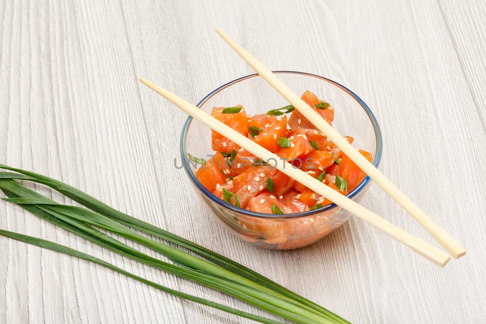 Hawaiian salmon poke with green onions and sesame seeds in glass bowl with chopsticks. Top view with copy space. Organic seafood.