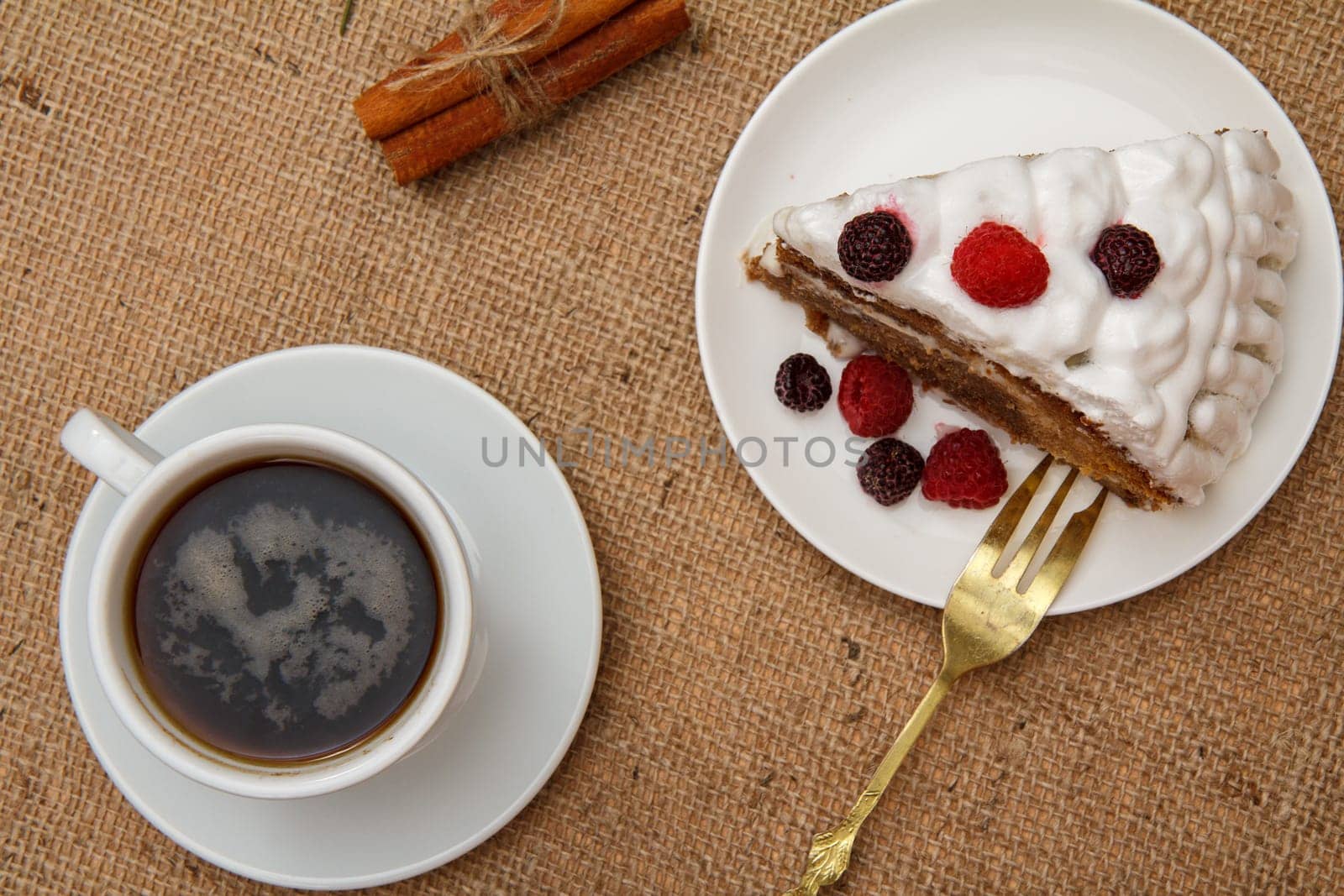 Cup of coffee, cinnamon, fork and slice of biscuit cake decorated with whipped cream and raspberries. by mvg6894