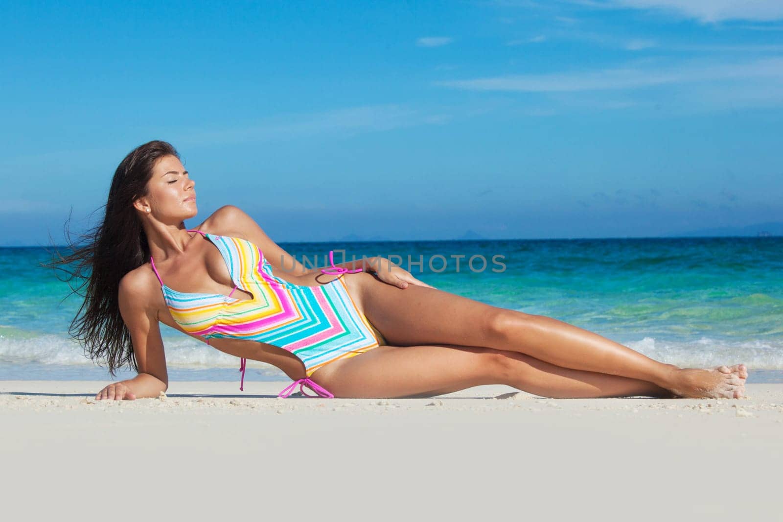 Beautiful woman in red swimsuit laying on sand at tropical beach