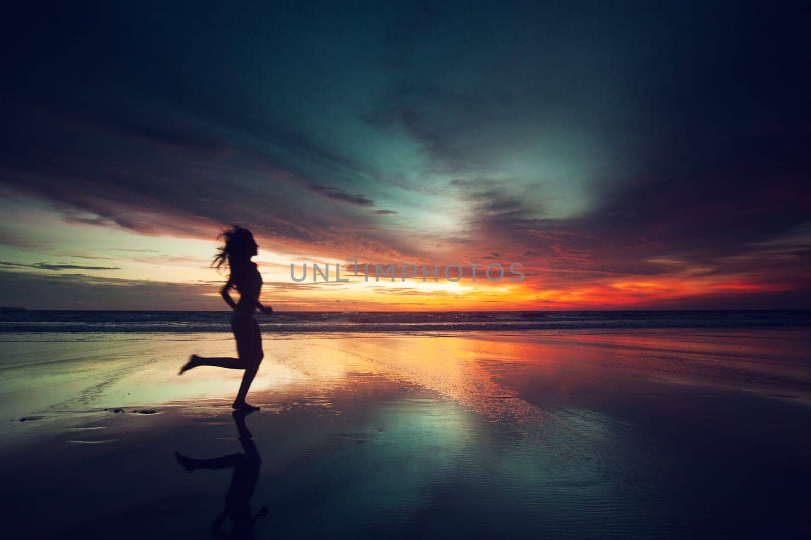 Woman running on the beach at sunset silhouette over sea and sky background