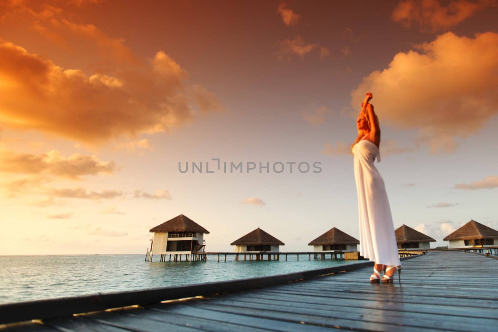 Woman in a dress on a bridge home sea and the maldivian sunset on the background