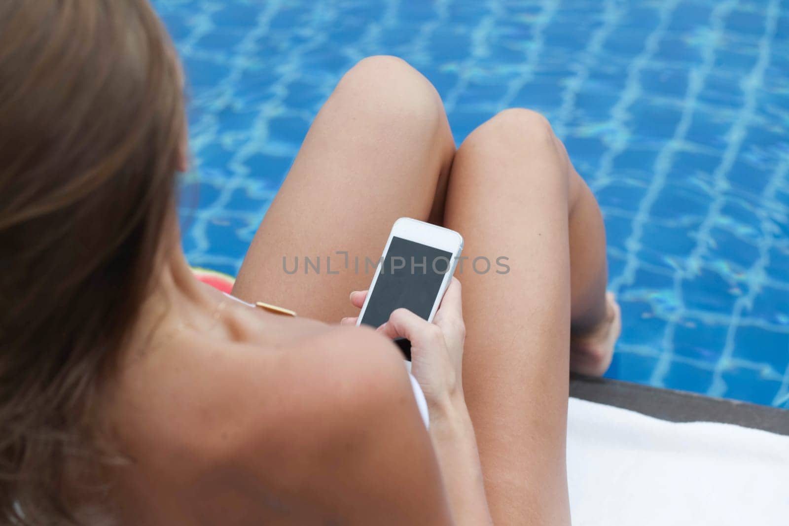 Woman using mobile phone by a pool by Yellowj