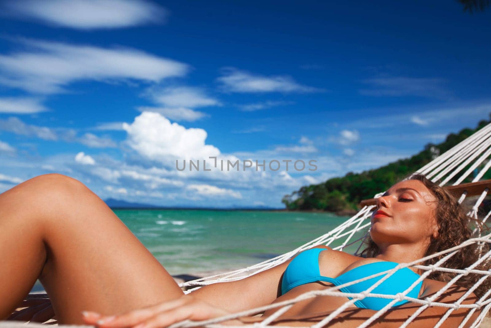 Young pretty woman laying in hammock on the beach. Enjoying the summer. Young woman swinging in hammock on tropical sea beach