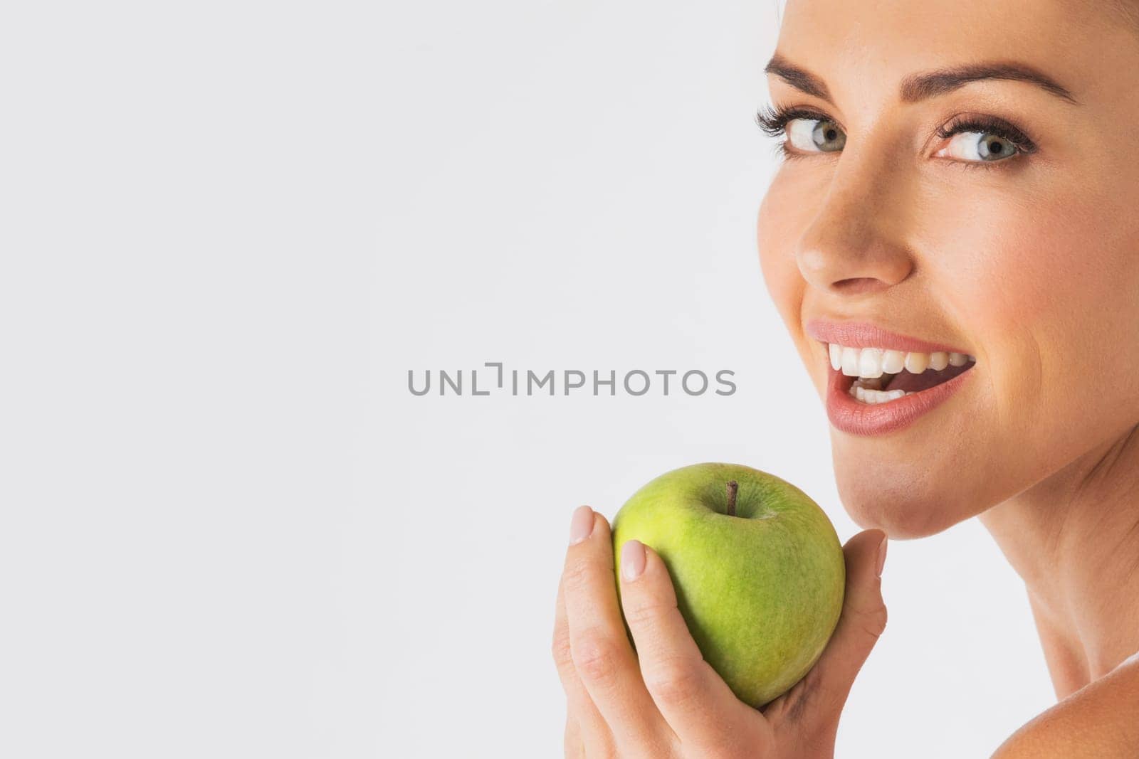 Beautiful smile, white strong teeth. Young woman with snow-white smile holding green apple