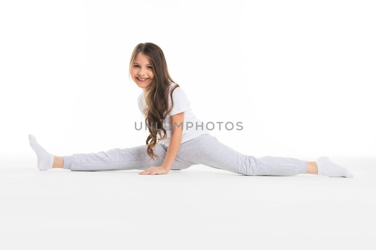 Little cute girl sitting in the splits, isolated on white background