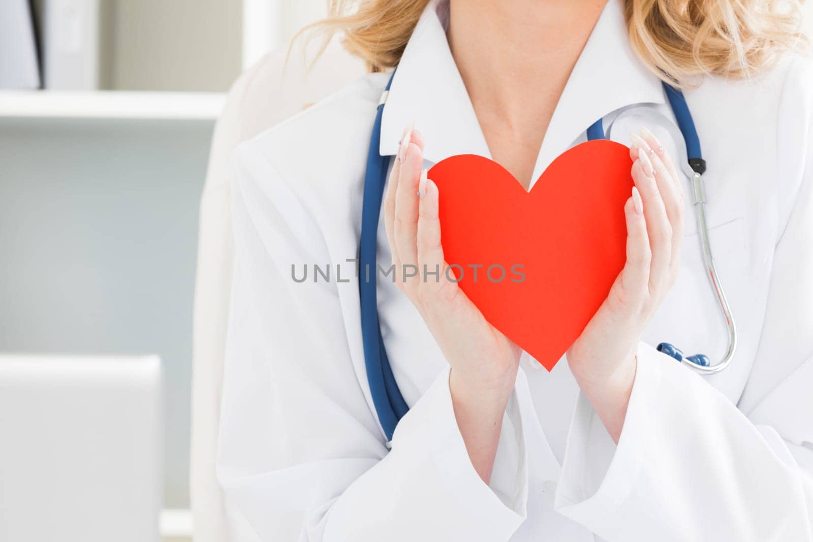 Close up of doctor in female white coat and stethoscope holding small red paper heart. CSR social responsibility, world health day, foster home, wellbeing, hope, Healthcare and cardiology concept