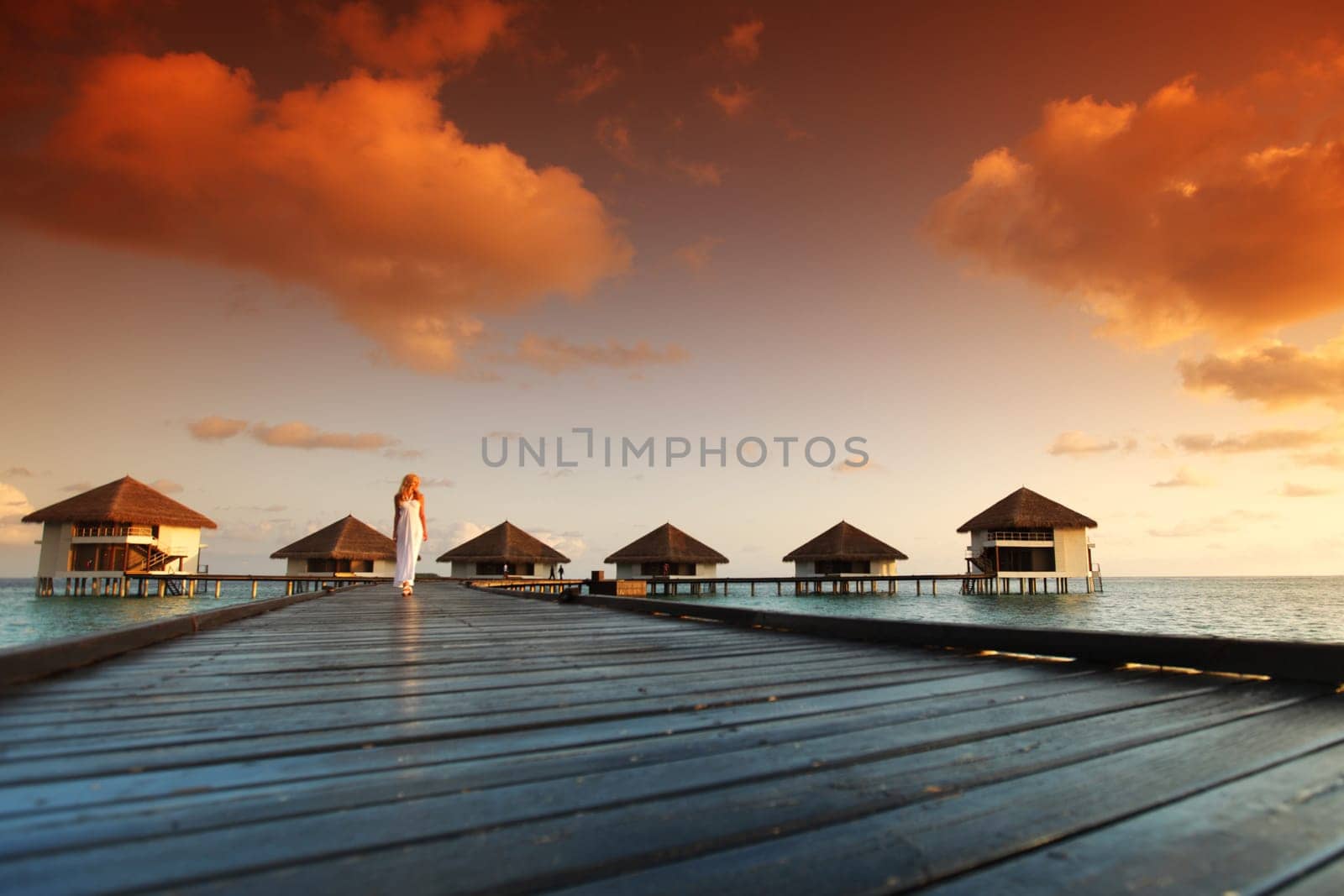 woman in a dress on a bridge home sea and the maldivian sunset on the background