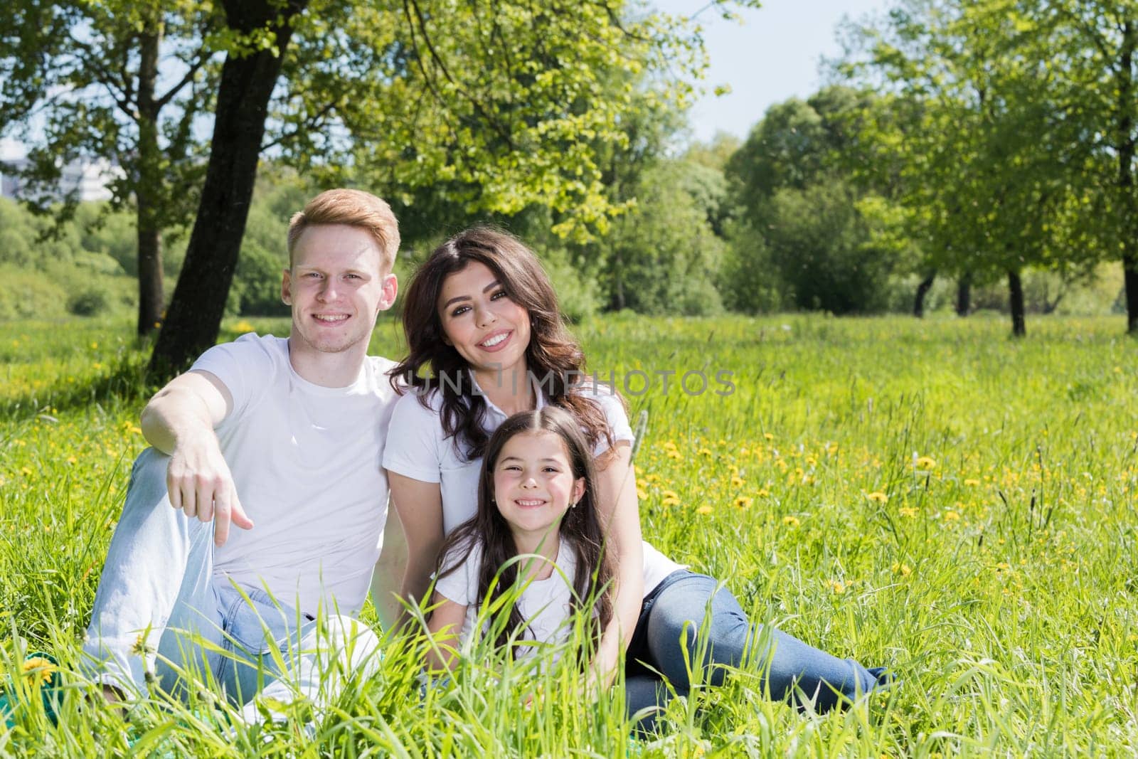 Happy smiling family of parents and daughter sitting on green grass in park