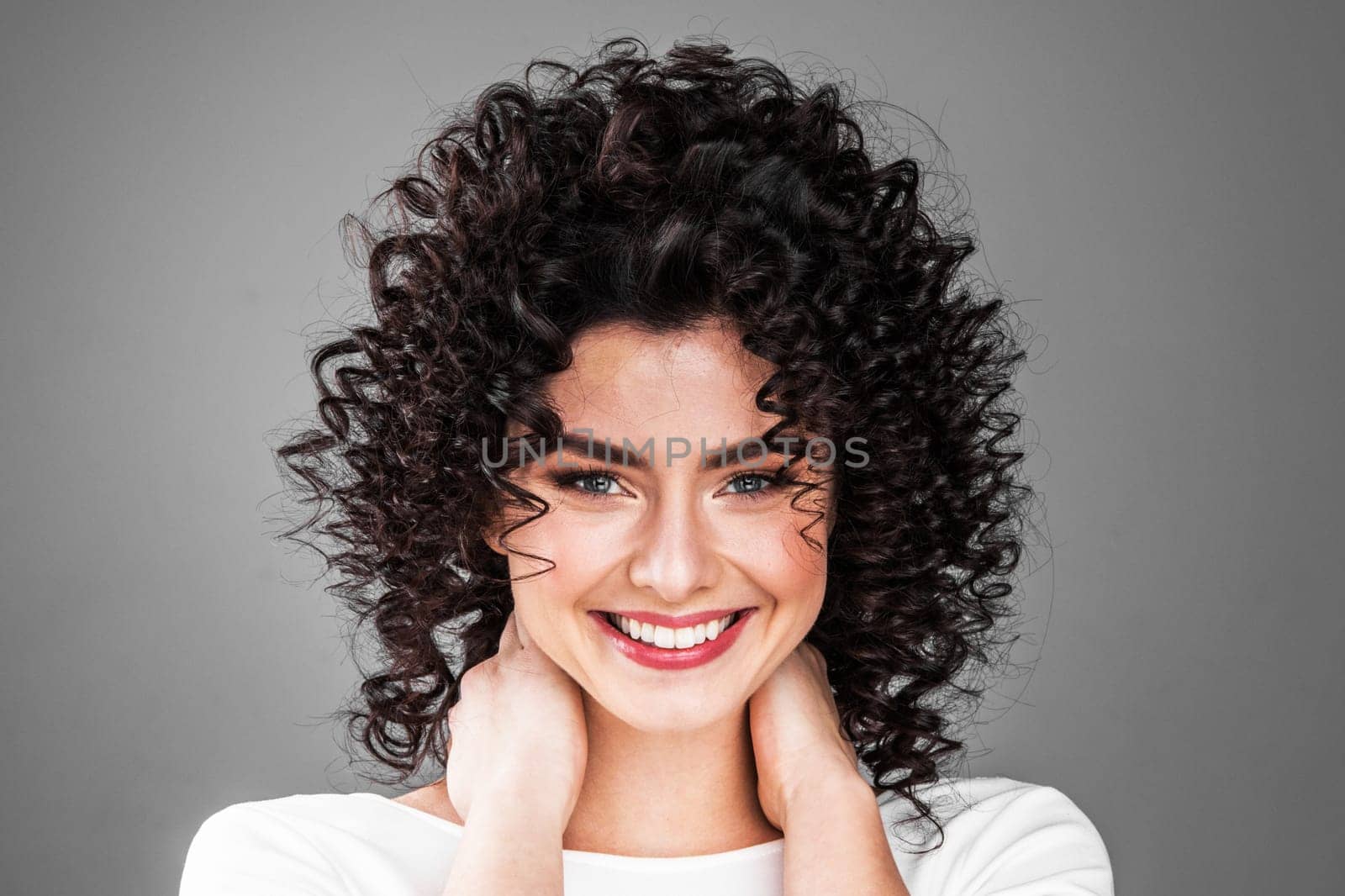 Portrait of amazing beautiful smiling woman with curly hair on gray background with copy space