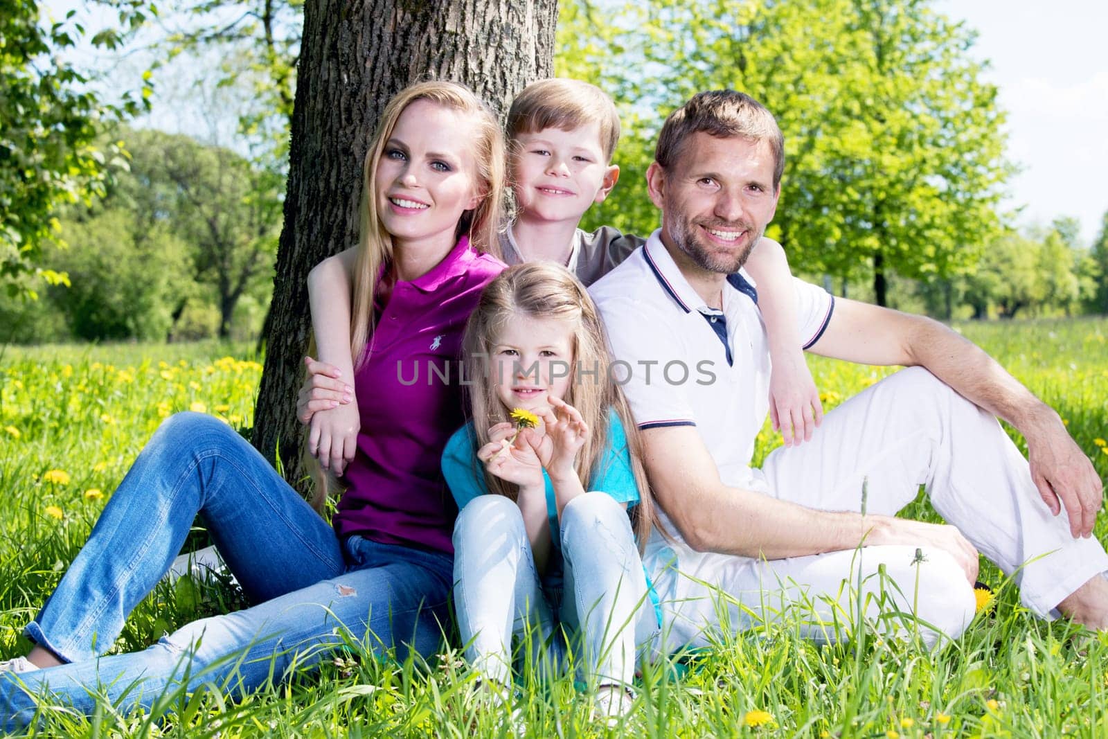 Happy family of parents and two children sitting on grass in spring park