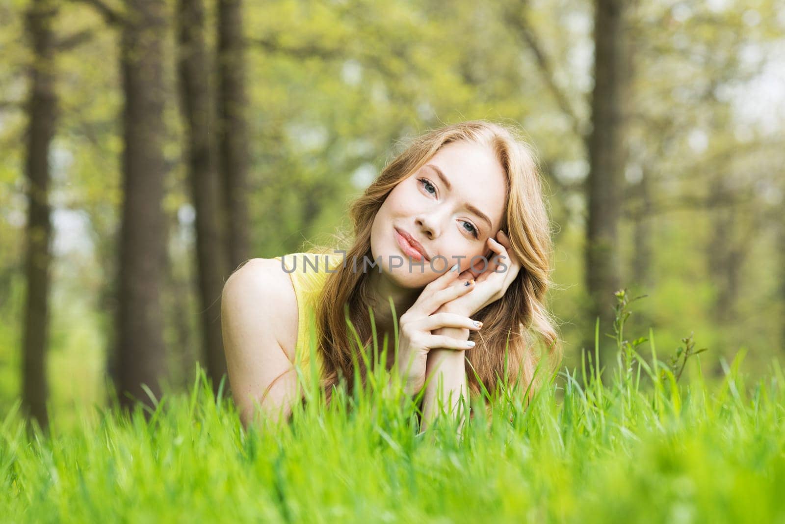 Happy smiling young woman laying on the green grass