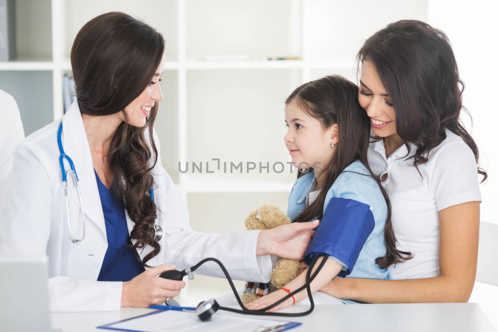 Young smiling female doctor and her little patient with teddy bear