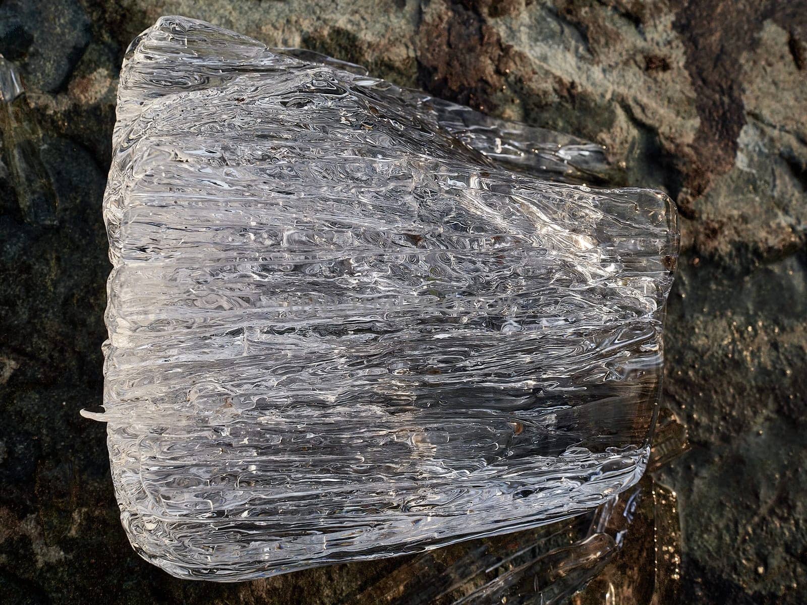 Natural crystal clear melting ice cubes on rock surface background. vertical