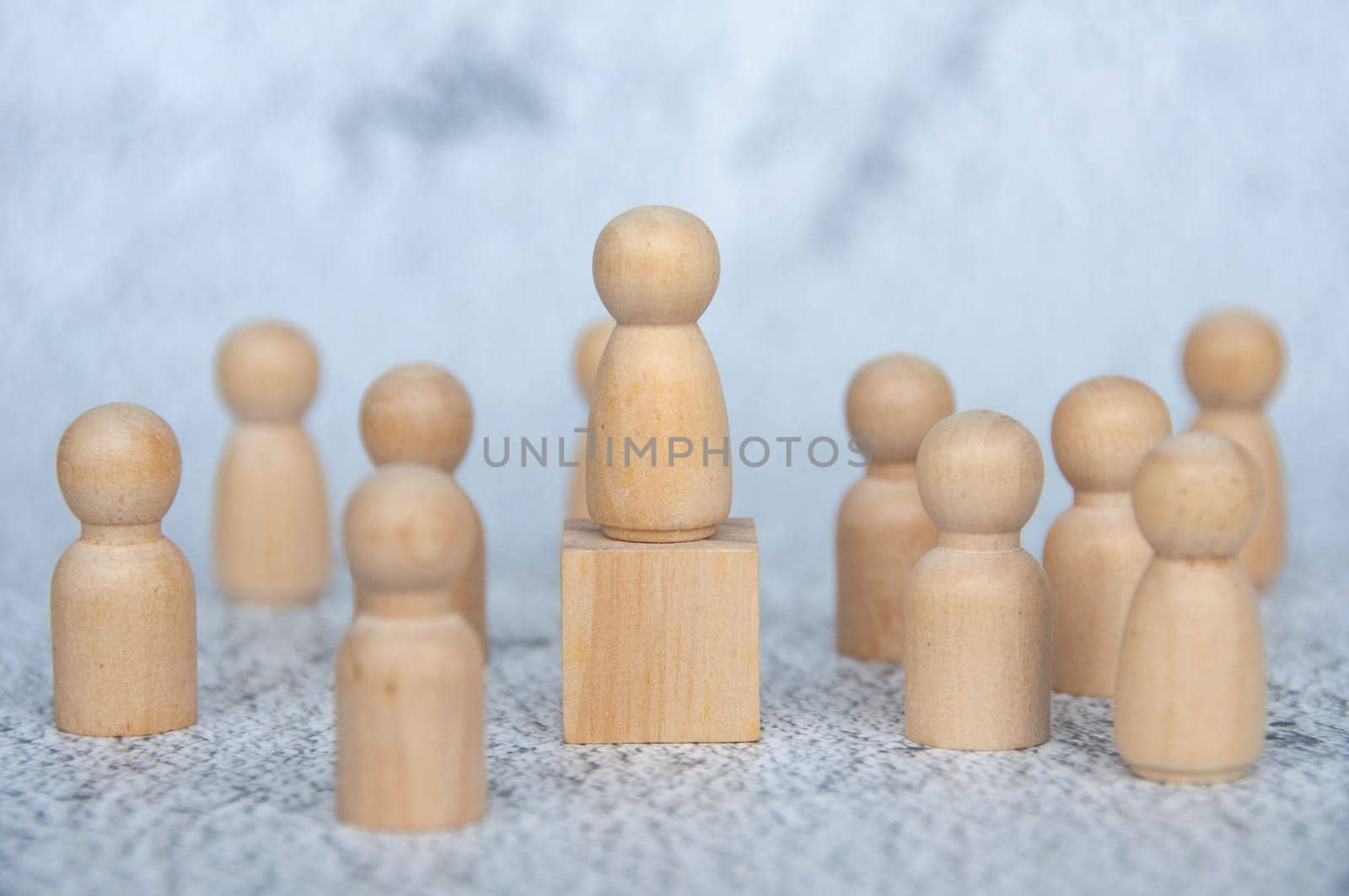 A wooden figure on top of wooden block representing a leader surrounded by other wooden figure. Leadership concept.