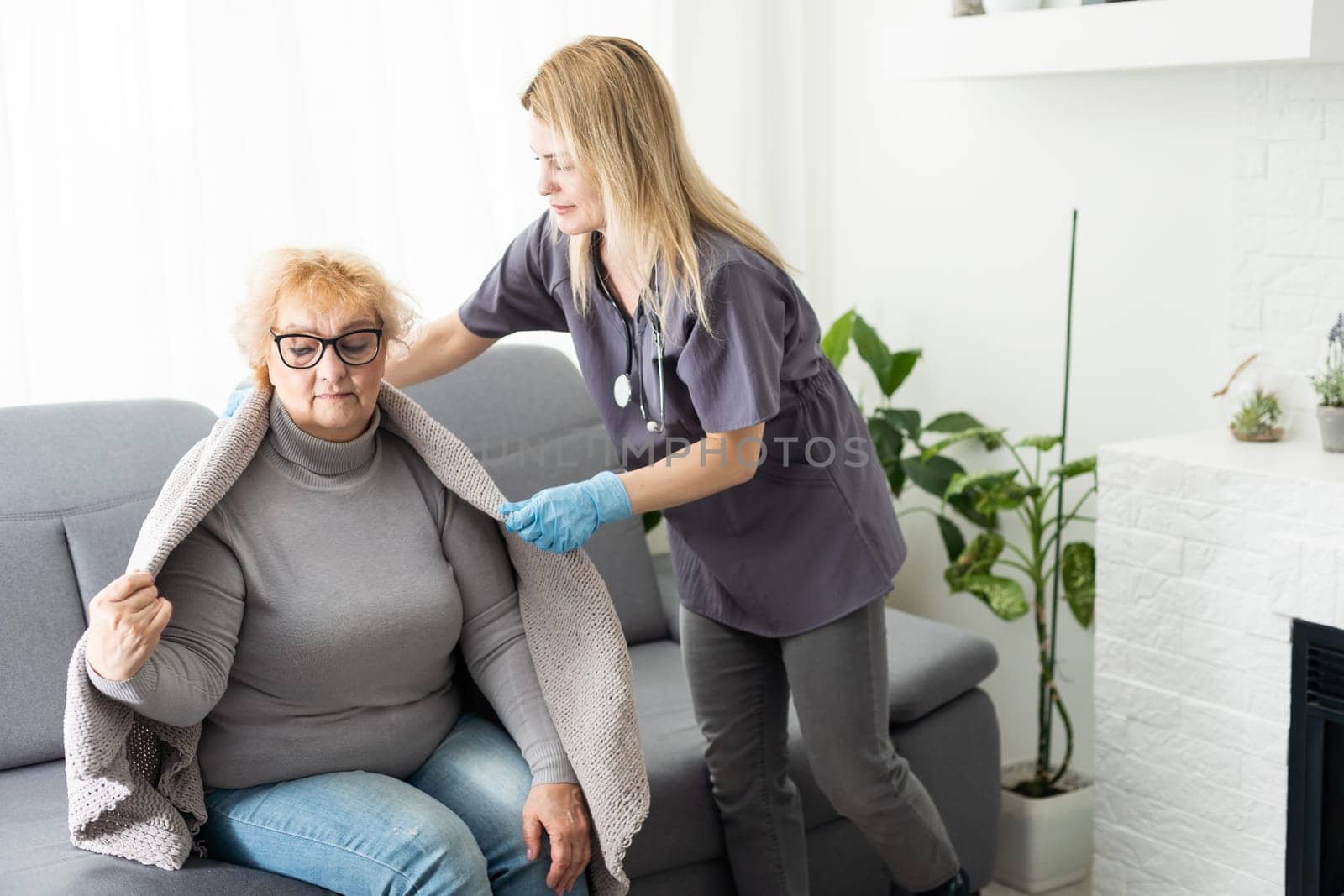 Mature female in elderly care facility gets help from hospital personnel nurse. Senior woman, aged wrinkled skin hands of her care giver. Grand mother everyday life. Background, copy space
