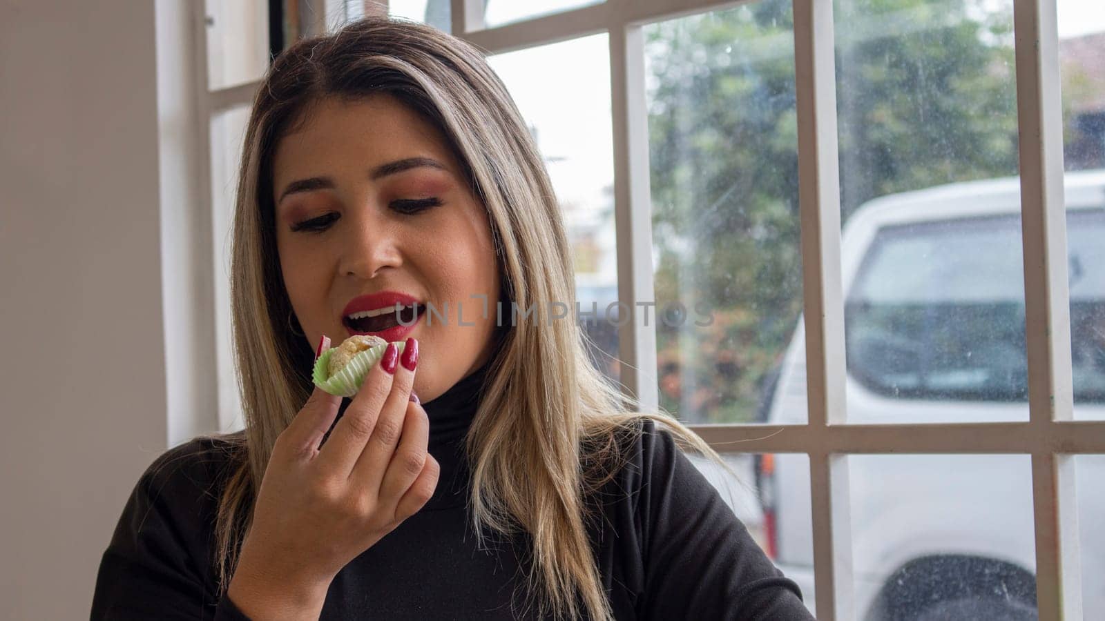 blonde girl sitting in a cafeteria looking at a cookie before placidly eating it. High quality photo
