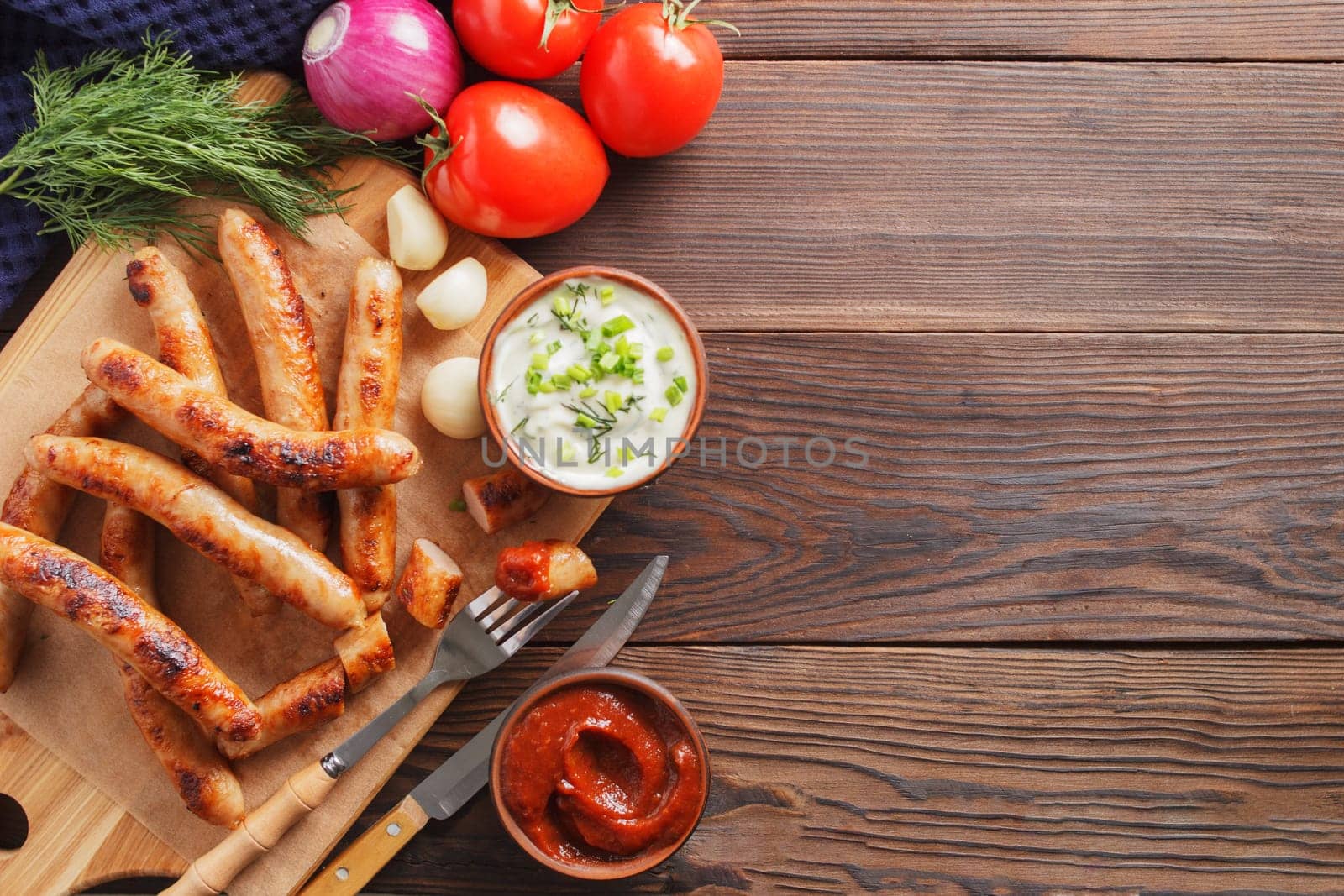 Delicious sausages on a wooden board with various sauces and fresh vegetables on a wooden table. copy space.