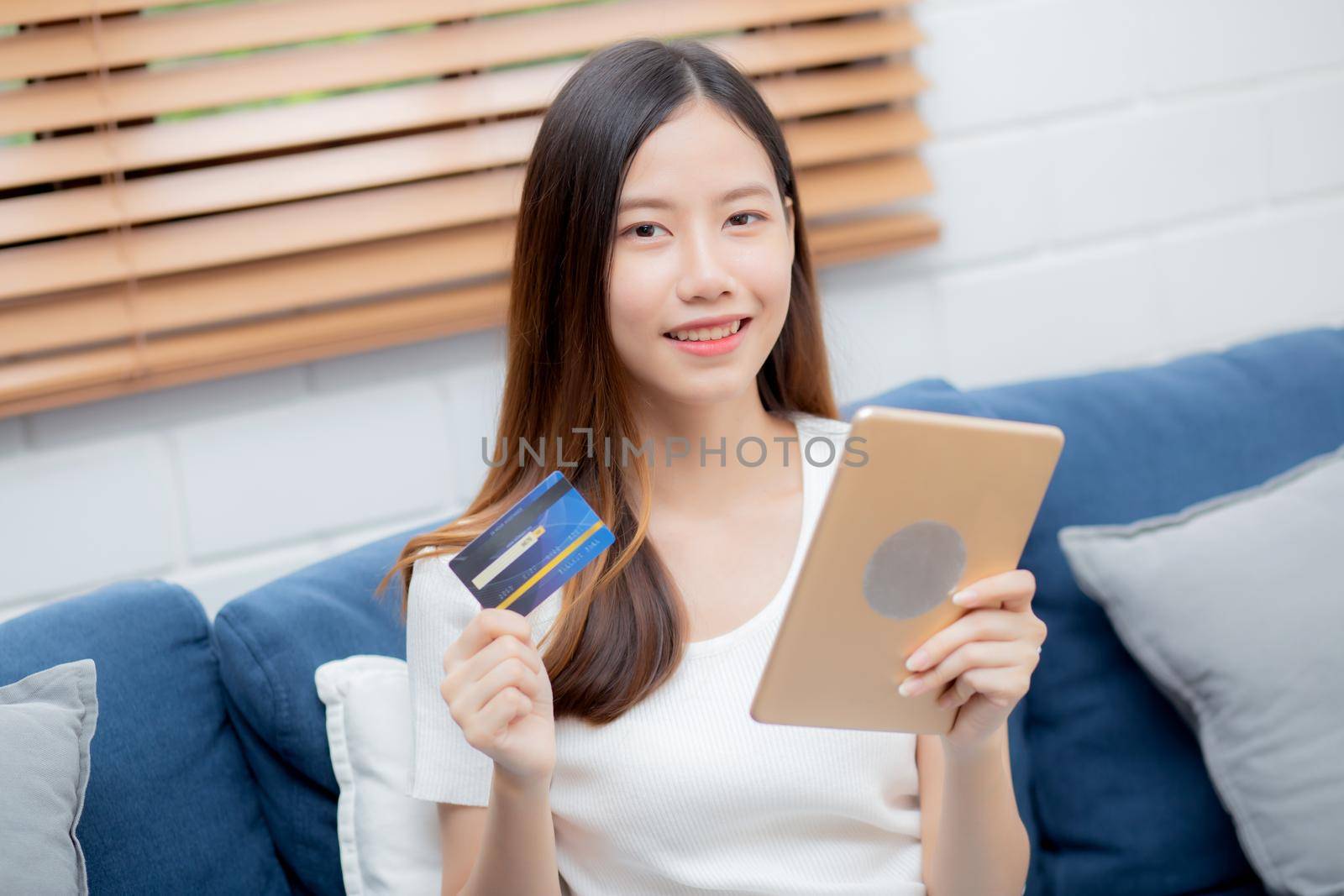 Young asian woman smiling holding credit card shopping online with tablet computer buying and payment, girl using debit card purchase or transaction of finance, lifestyle and e-commerce concept. by nnudoo