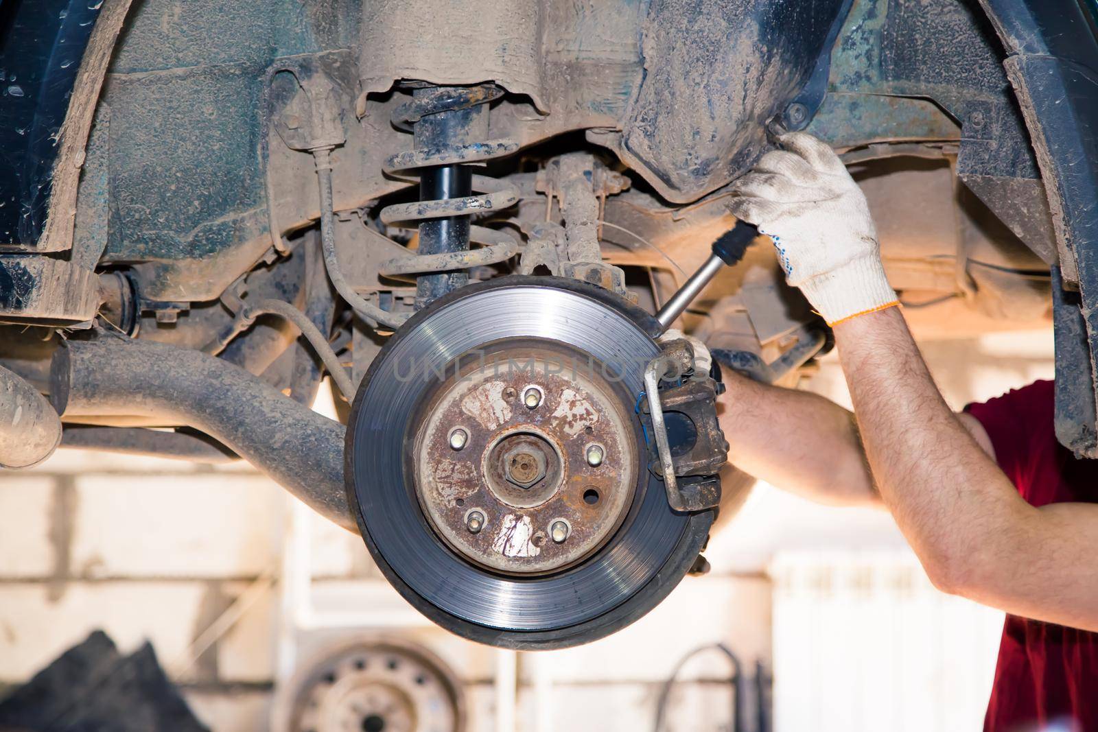 The man's hands remove the worn and rusty rear wheel caliper. In the garage, a person changes the failed parts on the vehicle. Small business concept, car repair and maintenance service.