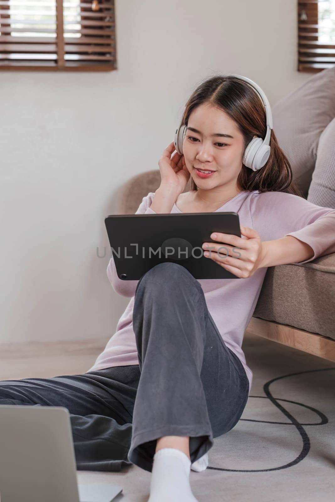 Confident asian woman listening to music with earphones and use tablet while relaxing of work in the office at home...