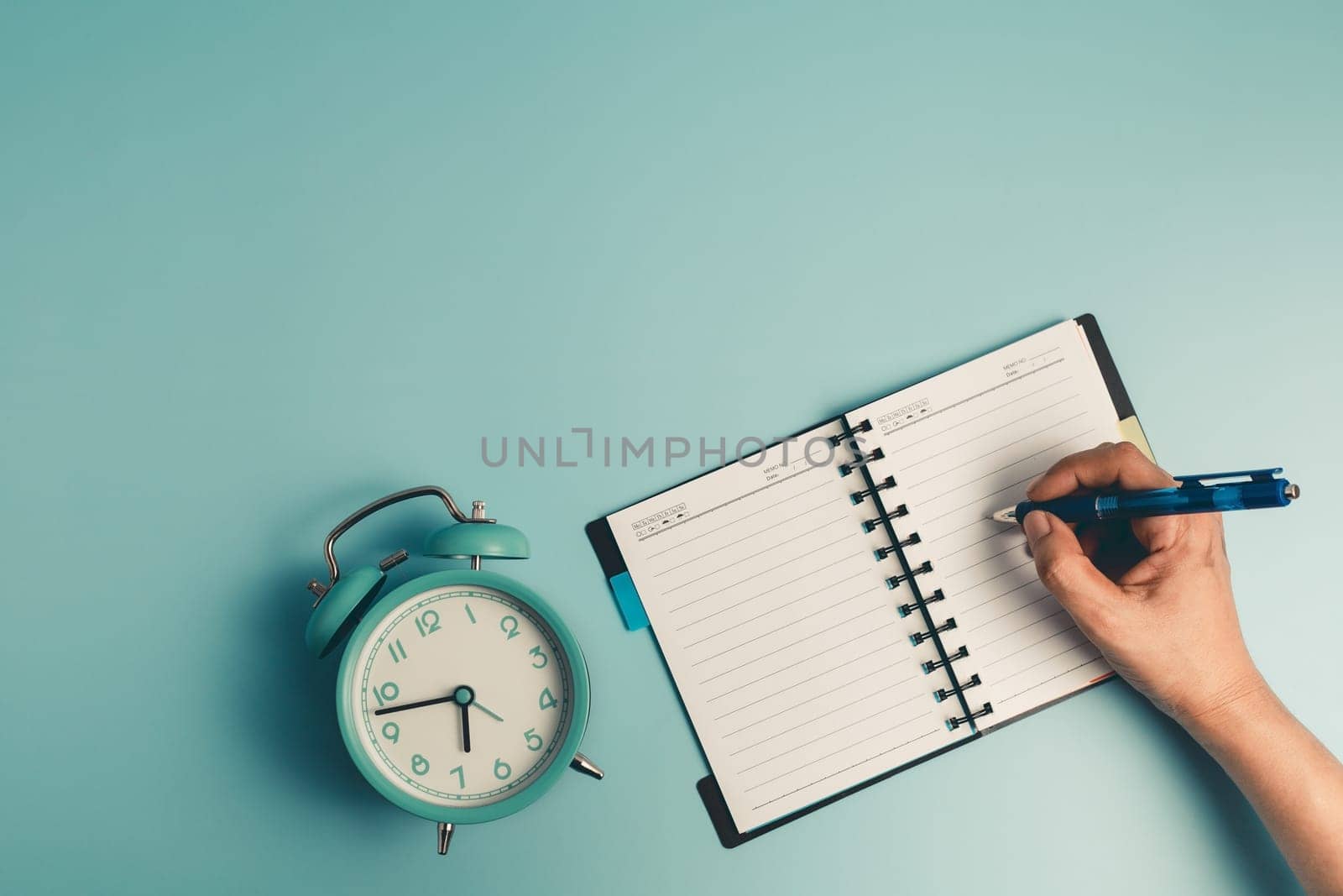 Hand writing on a dairy notebook with an alarm clock on blue background for the concept of work, study and time management.