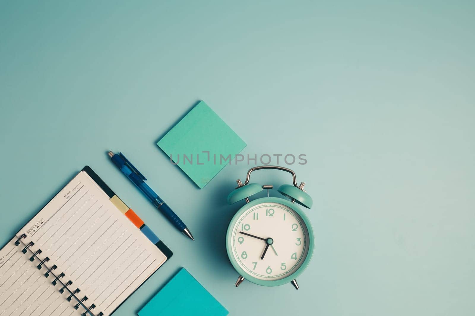 An alarm clock with a diary notebook and others work and educational materials on blue background for the concept of work, study and time management.