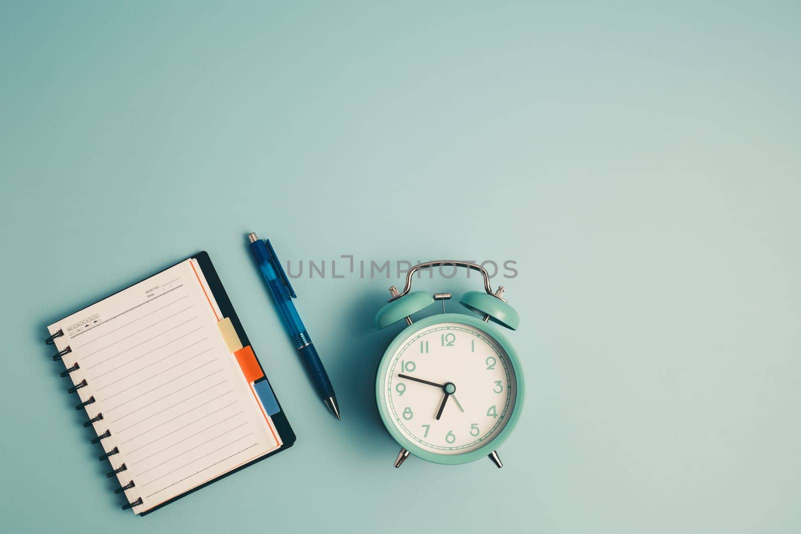 An alarm clock with a diary notebook and others work and educational materials on blue background for the concept of work, study and time management.