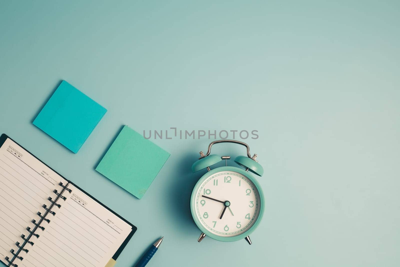 An alarm clock with a diary notebook and others work and educational materials on blue background for the concept of work, study and time management.