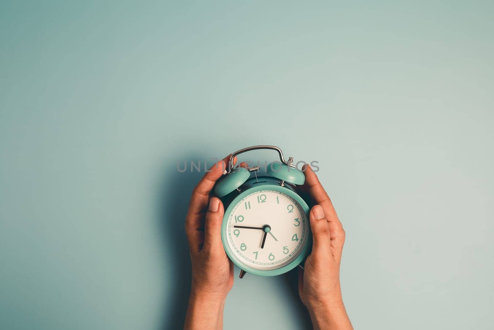 Hand holding an alarm clock on blue background for the concept of time management.