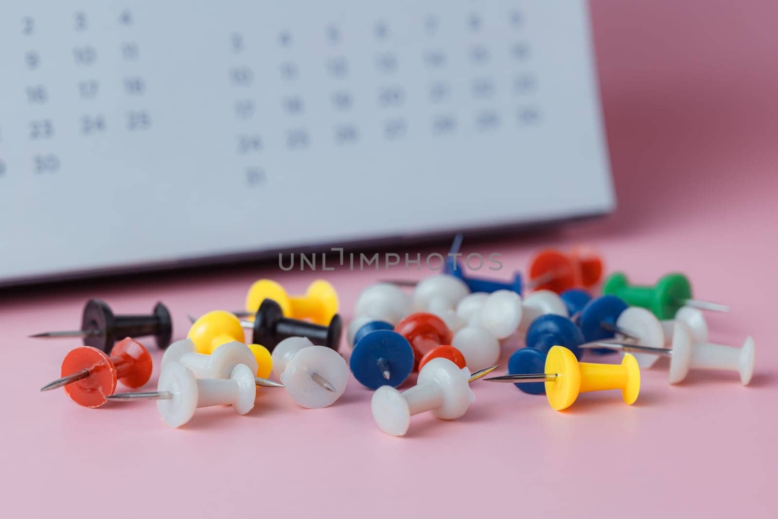 Push pins with blurred calendar on pink background for the concept of appointment, reminder and important note.