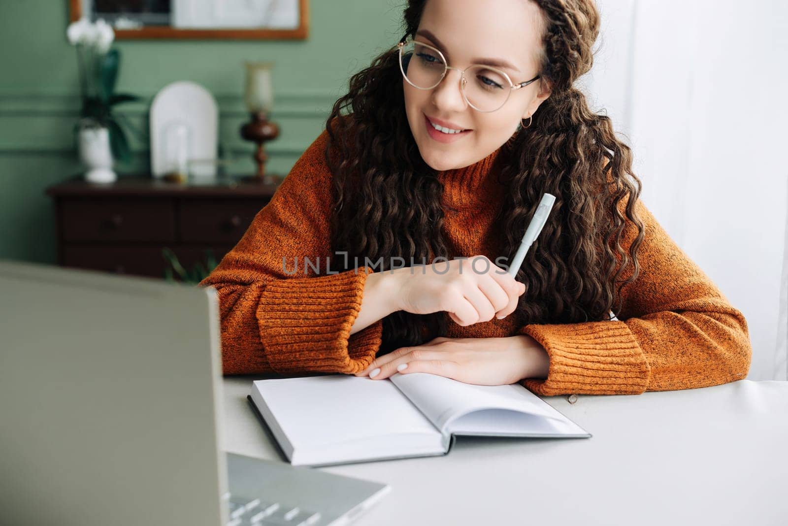 Young smiling pretty woman student using laptop elearning or remote working at home office using laptop computer watching webinar, learning web course, studying online sitting at table, writing notes