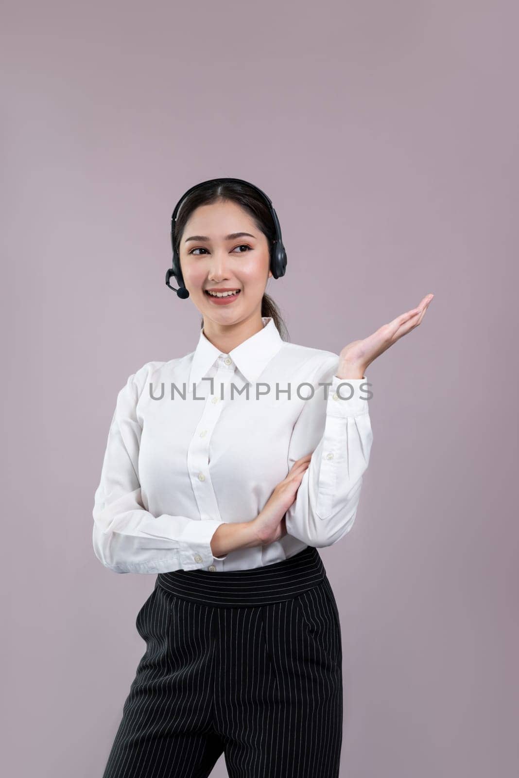 Asian female call center operator with smile face advertises job opportunity, wearing a formal suit and headset holding hand gesture for product on customizable isolated background. Enthusiastic